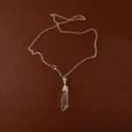 Handmade clear quartz point pendant on light neutral or white background