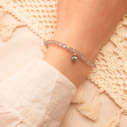 Woman wearing chalcedony charm bracelet, relaxed in a serene bedroom setting