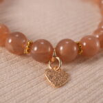 Close-up of the heart charm and smooth peach moonstone beads reflecting light