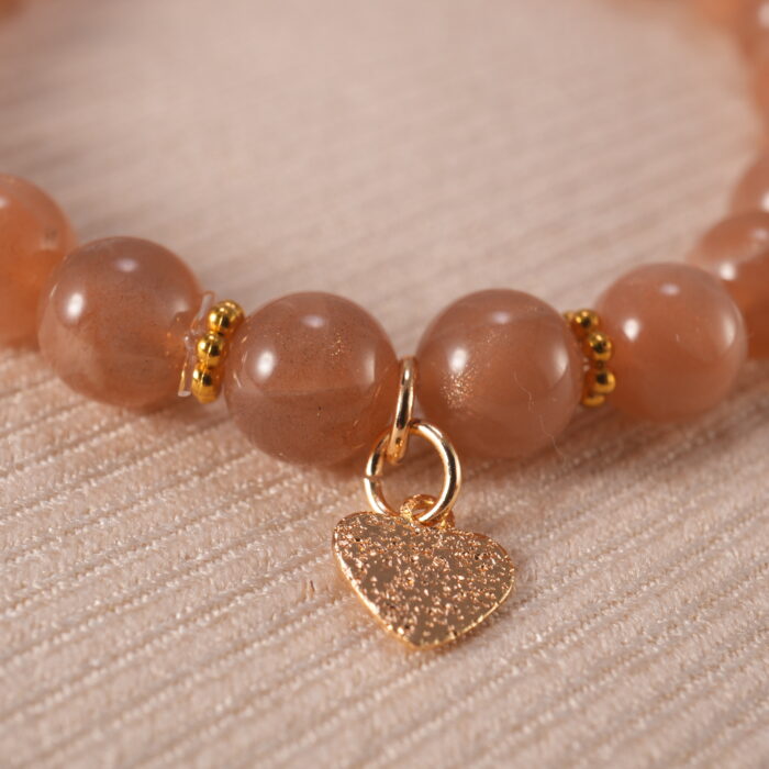 Close-up of the heart charm and smooth peach moonstone beads reflecting light