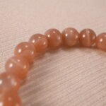 Close-up of the heart charm and smooth peach moonstone beads reflecting light