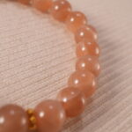 Close-up of the heart charm and smooth peach moonstone beads reflecting light