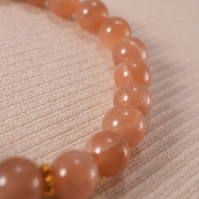 Close-up of the heart charm and smooth peach moonstone beads reflecting light