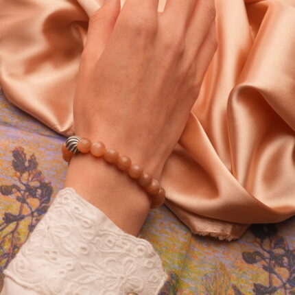 Worn by a relaxed hand in natural lighting, highlighting the soft peach tones and peaceful aura