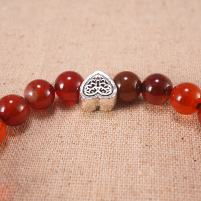 Close-up of red agate beads and silver heart charm on elastic cord