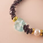 Close-up of polished garnet, lustrous pearl, and translucent aquamarine beads strung on durable elastic cord.