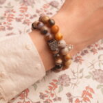 Model wearing stacked earthy and cool-toned gemstone bracelets.