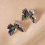 A pair of butterfly-shaped moonstone stud earrings on a white background, displaying a soft iridescent glow.