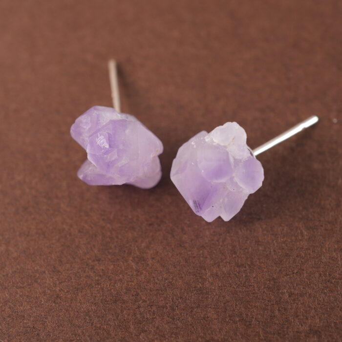 A pair of raw amethyst stud earrings displayed on a plain background, highlighting their natural and rustic texture.